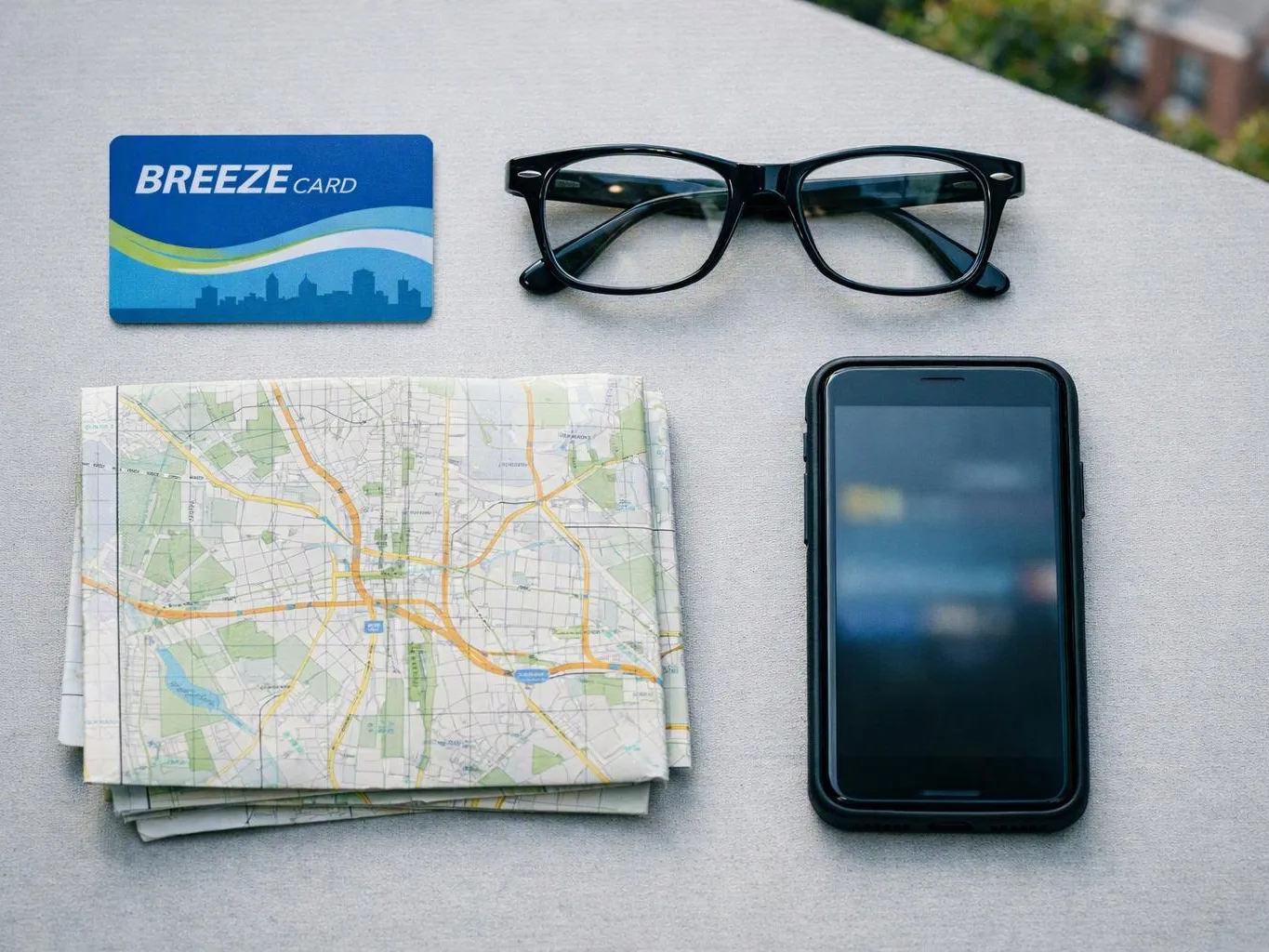 A card, eyeglasses, folded map, and smartphone rest on a light gray table