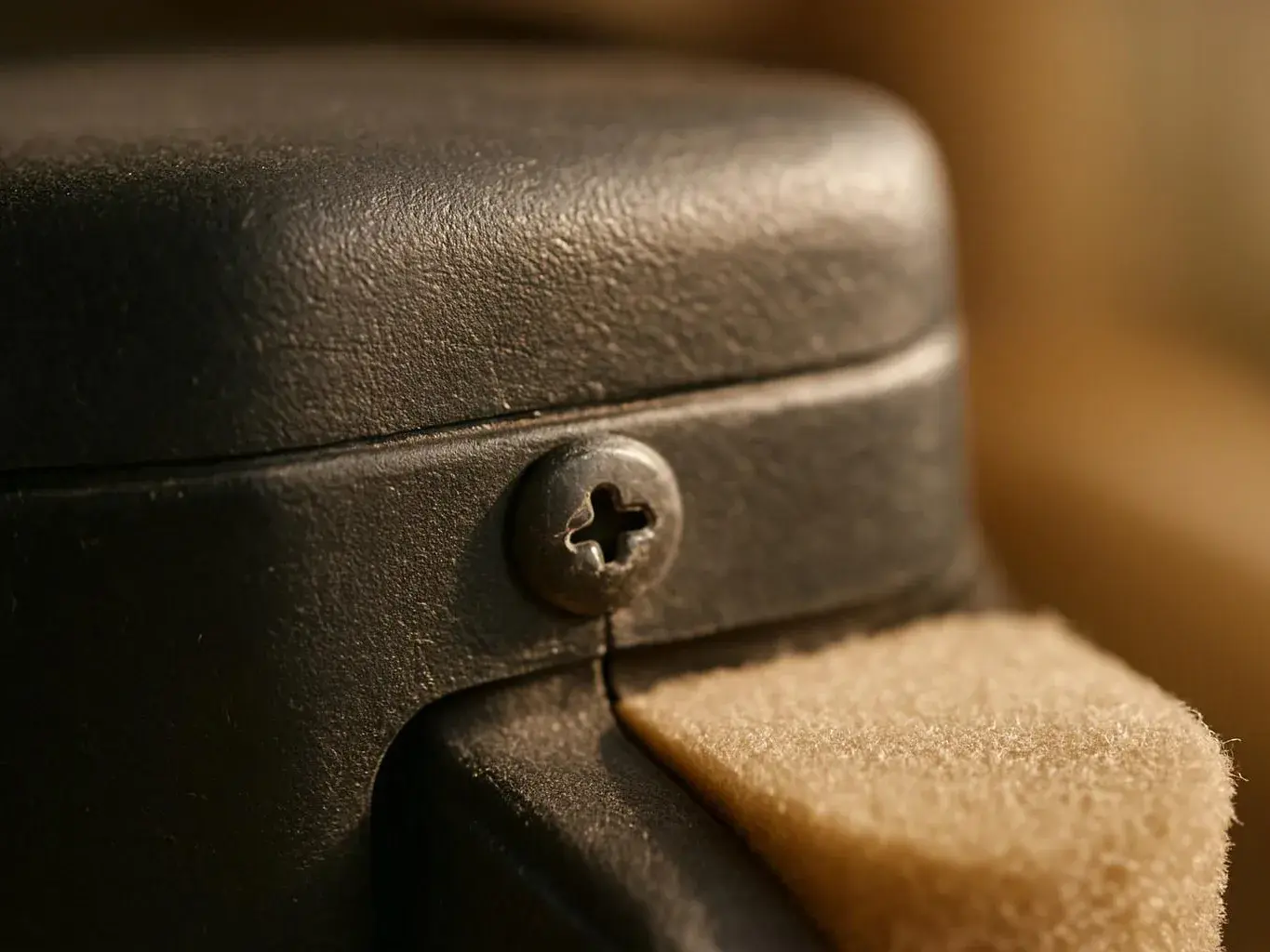 Close-up of a black plastic casing with a screw beside a beige felt pad against a blurred warm background